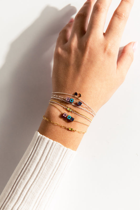 A person's wrist showcasing multiple bracelets with various charms, including hearts and flowers, in gold and silver colors.
